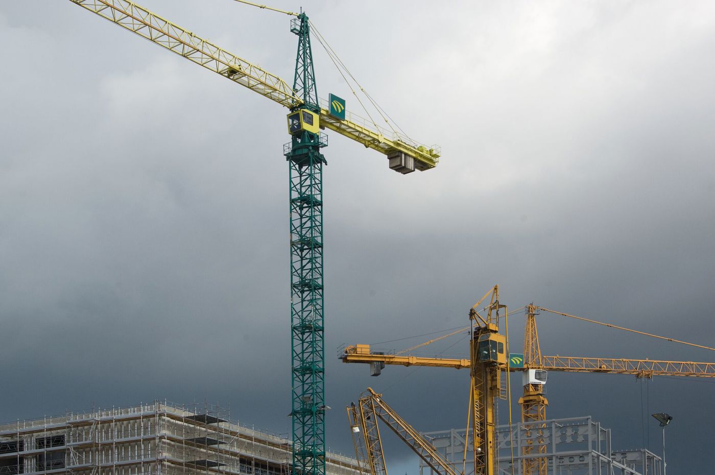 Meerdere bouwkranen bij een nieuwbouwproject onder een bewolkte lucht