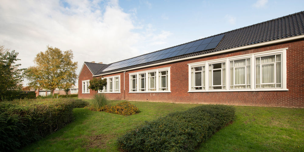 Een verdiepingsgebouw met zonnepanelen op dak en een groene tuin
