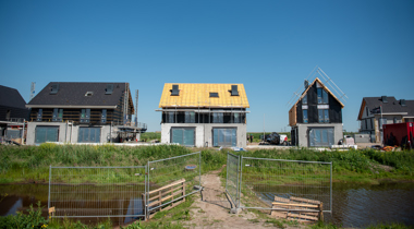 Huizen in aanbouw aan een vaart met bouwhekken op de voorgrond.