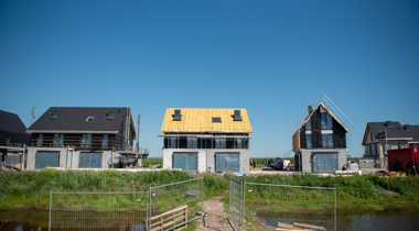 Huizen in aanbouw aan een vaart met bouwhekken op de voorgrond.