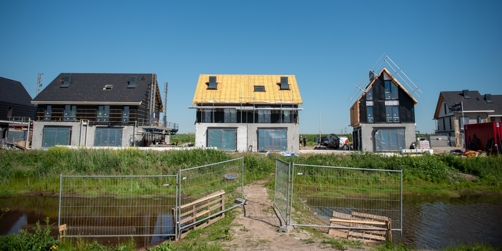 Huizen in aanbouw aan een vaart met bouwhekken op de voorgrond.
